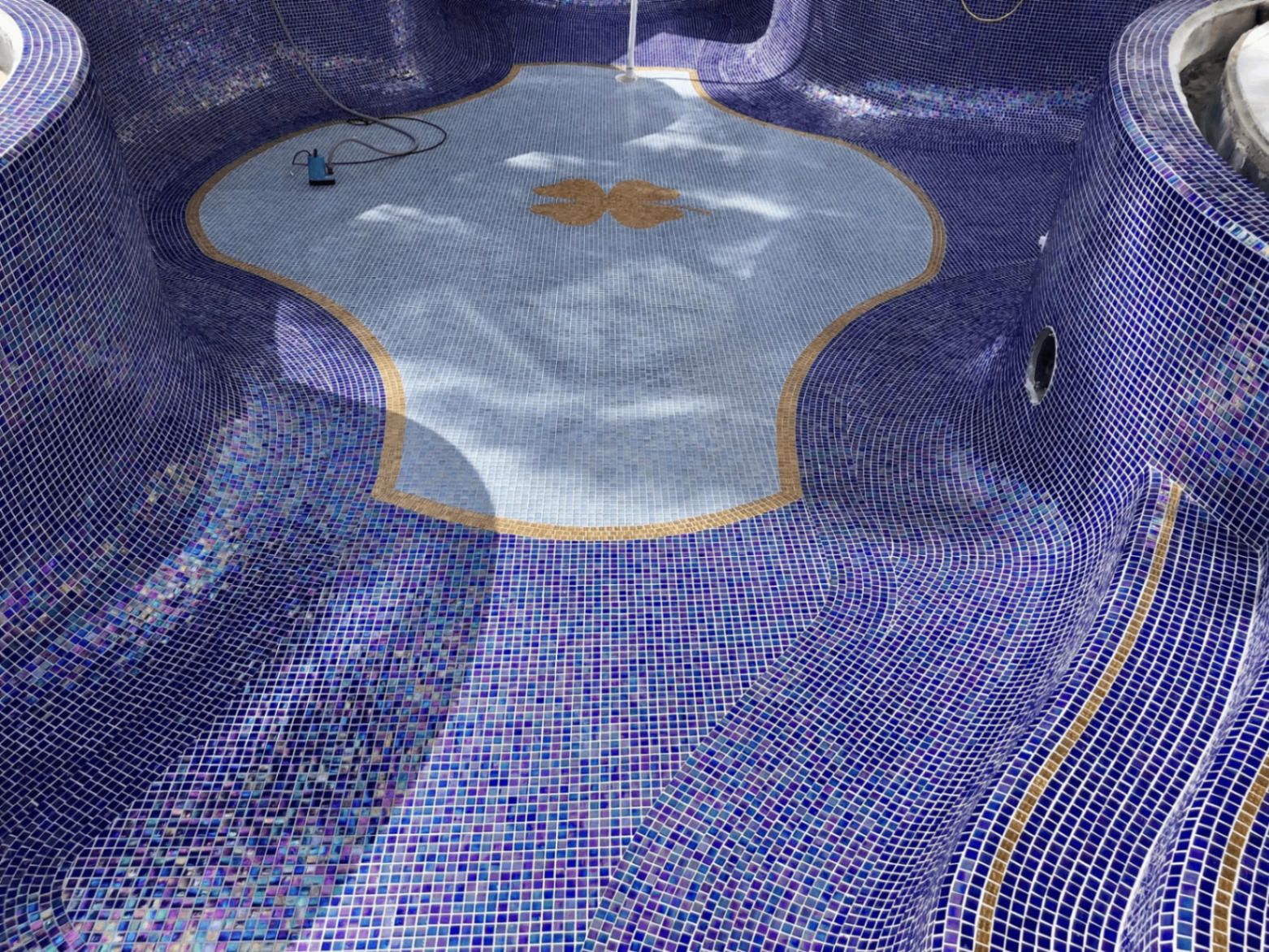 Interior of iridescent blue mosaic pool with custom shell inlay